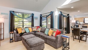 Een ruime woonkamer met een hoekbank, een eethoek en een keuken op de achtergrond.