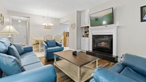 Un salon avec des canapés en cuir bleu, une table basse en bois, une cheminée et un téléviseur fixé au-dessus.