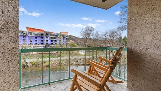 Un balcon avec un fauteuil à bascule en bois, une rambarde verte et une vue sur un immeuble en construction.