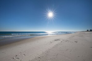 En strand med fodspor, der fører ned til vandet, en klar himmel og en strålende sol.