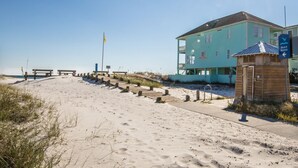 A beachside building with a clear path leading to the beach, a flag, and a sign indicating beach access.
