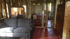 A rustic room with exposed wooden beams, a grey sofa, a patterned rug, and a dining area with a table and chairs. - 4 Bedroom Private vacation home in Montpezat (Montpezat)