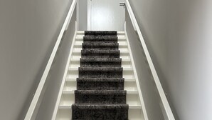 Una escalera con escalones de mármol oscuro y barandillas blancas, que lleva a una puerta en la parte superior.