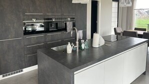 Una cocina moderna con armarios oscuros, una isla grande con lavamanos e iluminación colgante.
