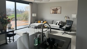 Una sala de estar moderna con un sofá gris, una silla negra y un comedor con una mesa y sillas.