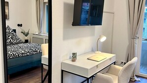 Une chambre à coucher avec un lit, un bureau, une chaise, un téléviseur et une fenêtre avec des rideaux.
