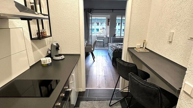 Une cuisine compacte dotée d’un plan de travail noir, d’une cuisinière intégrée et d’un petit coin repas avec deux chaises.