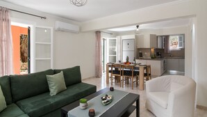 Ein modernes Wohnzimmer mit einem grünen Sofa, einem weißen Sessel und einem Essbereich mit einem Holztisch und Stühlen.