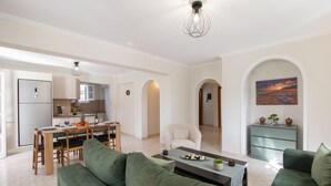 Ein modernes Wohnzimmer mit grünen Sofas, ein Essbereich mit Holztisch und -stühlen, und eine Küche im Hintergrund.
