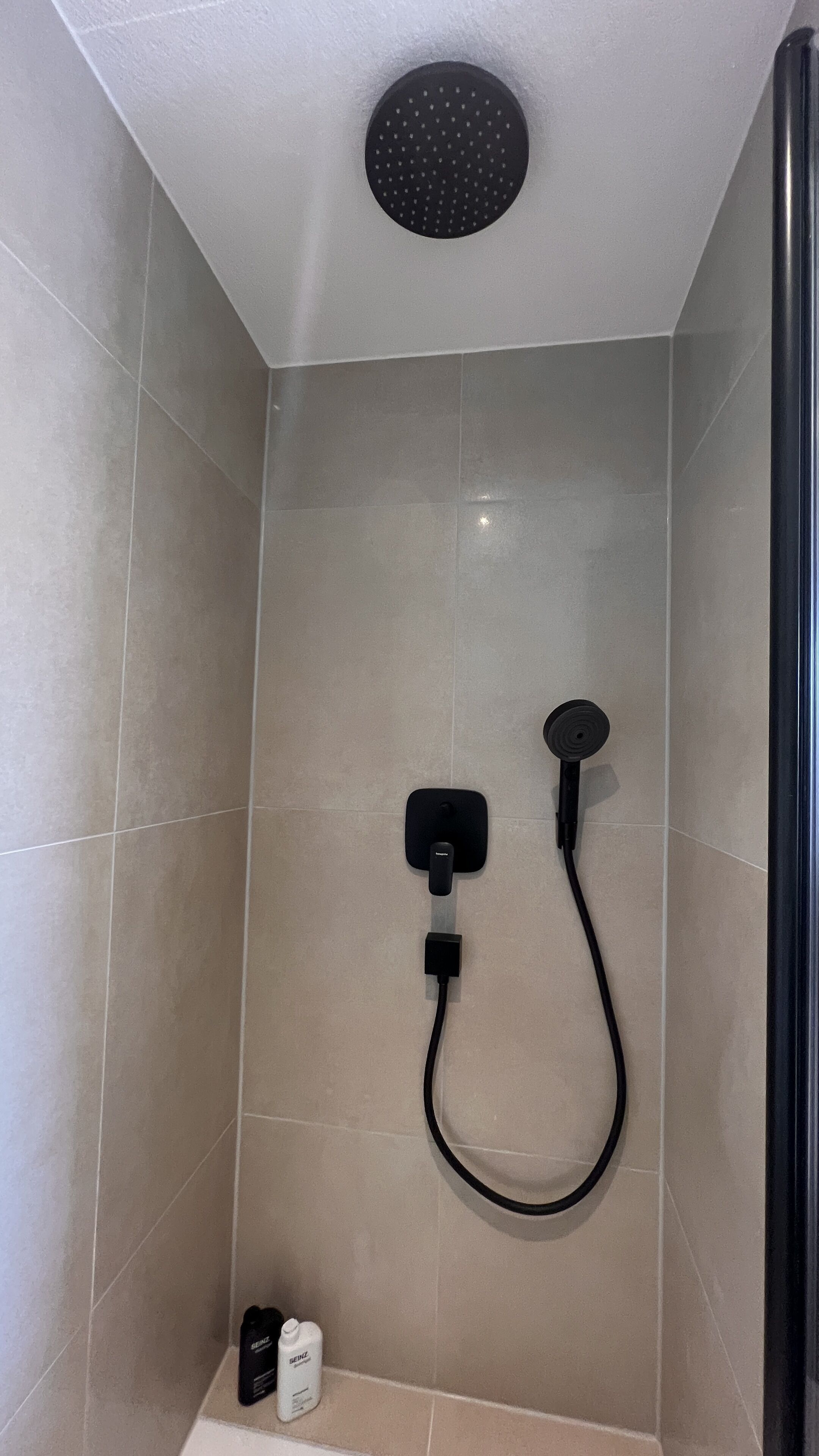 Un espace douche équipé d’un pommeau de douche noir à main et d’un panneau de commande fixé au mur.