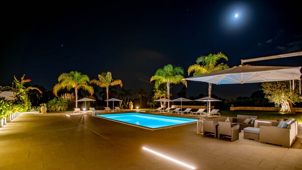 A nighttime pool area with a clear pool, lounge chairs, umbrellas, and a moon in the sky. - Villa With Private Pool Terraforte Suites Wellness Activities (Marina di Ragusa)
