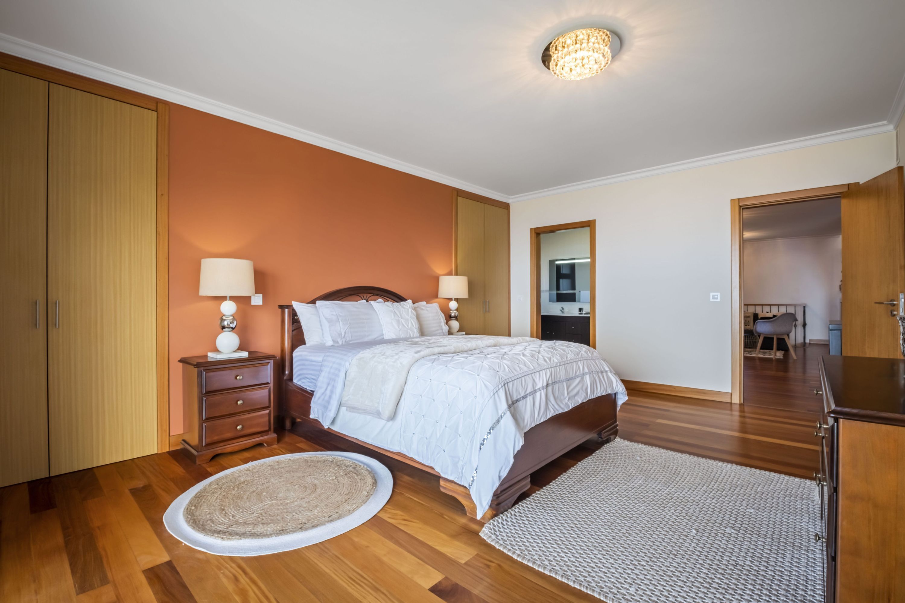 A bedroom with a bed, nightstands, a dresser, a round rug, and a ceiling light fixture.