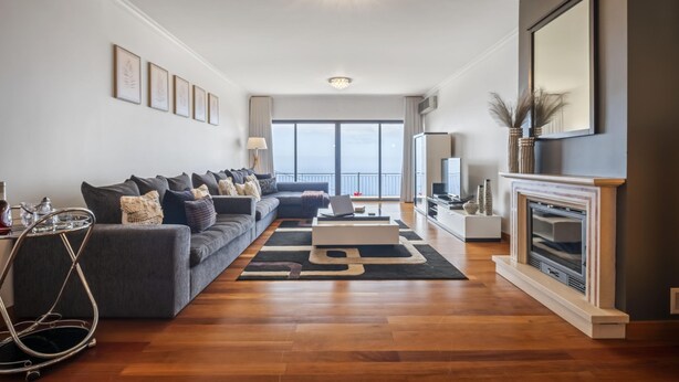 Ein modernes Wohnzimmer mit einem grauen Sofa, einem Kamin und einem großen Fenster mit Blick ins Freie.