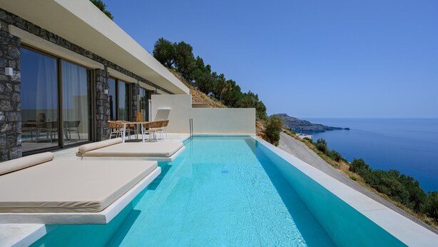 A modern poolside area with a clear view of the sea, a stone facade, and a seating area with a table and chairs. - Pyrgos Exquisite villa 3 ,private pool,South Crete (Plakias)