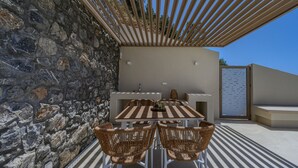 An outdoor patio with a stone wall, a wooden pergola, a table with chairs, and a built-in bench. - Pyrgos Exquisite villa 3 ,private pool,South Crete (Plakias)