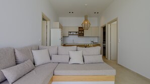 A modern living room with a grey sectional sofa, a wooden coffee table, and a kitchen in the background. - Pyrgos Exquisite villa 3 ,private pool,South Crete (Plakias)