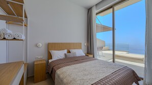 Una habitación de hotel moderna con una cama grande, cabecera de madera y vista al mar a través de una puerta corrediza de vidrio.