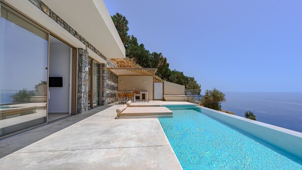 Un área moderna junto a la piscina con vista despejada al mar, un espacio de descanso cubierto y fachada de piedra.