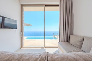 A room with a bed, a TV, and a sliding glass door leading to a beach view. - Pyrgos Exquisite villa 5 ,private pool,South Crete (Plakias)