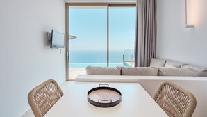 A modern room with a large sliding glass door leading to a balcony, a white table with a tray, two wicker chairs, a sofa, and a mounted television. - Pyrgos Exquisite villa 5 ,private pool,South Crete (Plakias)