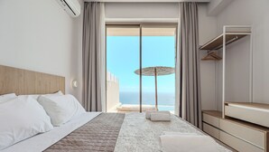 A modern hotel room with a bed, a large window with curtains, a view of the sea, and a balcony with an umbrella. - Pyrgos Exquisite villa 5 ,private pool,South Crete (Plakias)