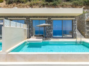 Zona de piscina con pared de piedra, una silla de descanso y una sombrilla.