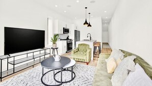 Una sala de estar moderna con televisor de pantalla plana, una mesa de centro redonda, un sofá y una zona de cocina al fondo.
