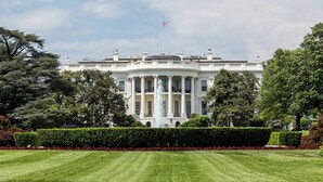 Un gran edificio neoclásico blanco con una cúpula central y columnas, rodeado de céspedes cuidados y árboles.