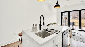 Una cocina moderna con una isla central, lámparas colgantes negras y un amplio ventanal.
