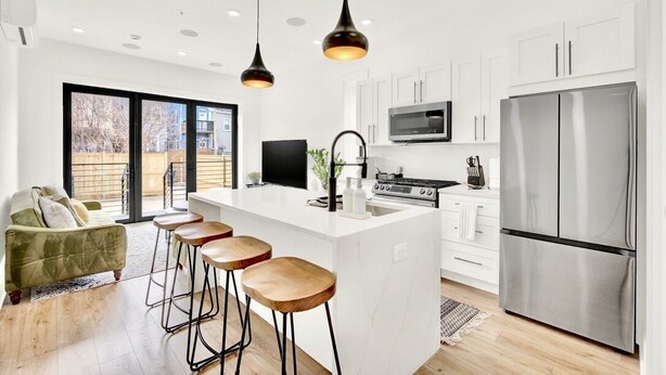 Una cocina moderna con armarios blancos, un refrigerador de acero inoxidable, una isla grande con taburetes e iluminación colgante.