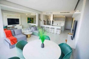 A modern living room with a sofa, a round table, and a green plant. There is a kitchen area with a bar and a dining table. - Náutico: Hermosa Vista al Muelle (Puerto Vallarta)