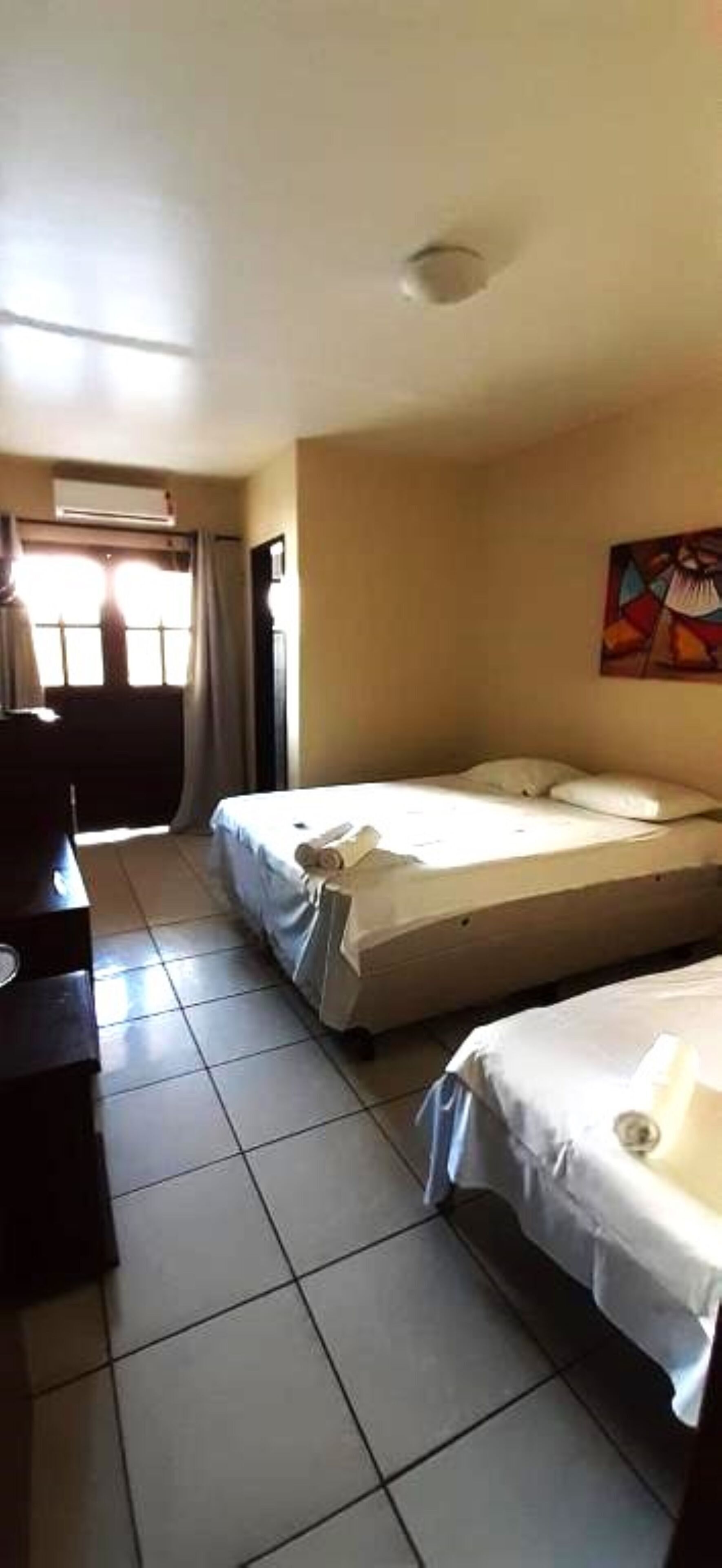 A hotel room with two beds, a desk, and a window with curtains.