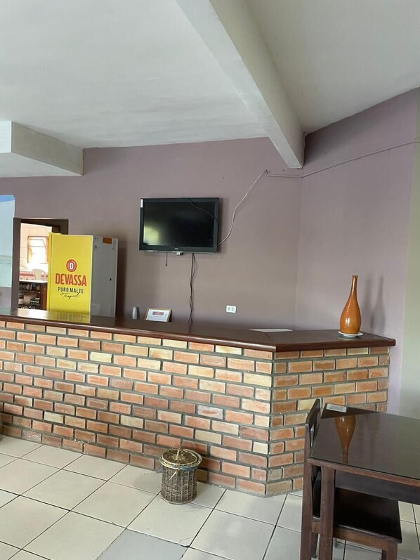 Un espace d’accueil avec un comptoir en briques, un téléviseur à écran plat fixé au mur et une enseigne indiquant « DEVASSA PURO MALTE ».