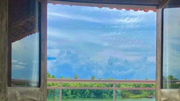 A room with a bed, two rolled towels, and a window overlooking a body of water and greenery. - Hotel Beira Rio Preguiças (Barreirinhas)