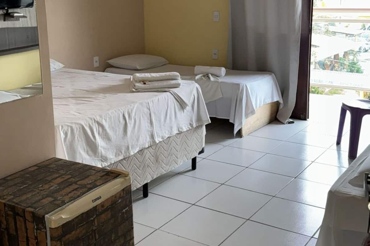 Une chambre d’hôtel avec deux lits, une petite table, une boîte décorée d’un motif en briques et une fenêtre avec un rideau.