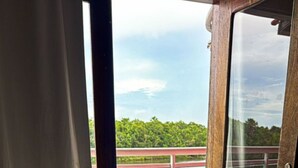 A hotel room with a bed, a rolled towel, and a view of a pool and greenery through an open door. - Hotel Beira Rio Preguiças (Barreirinhas)