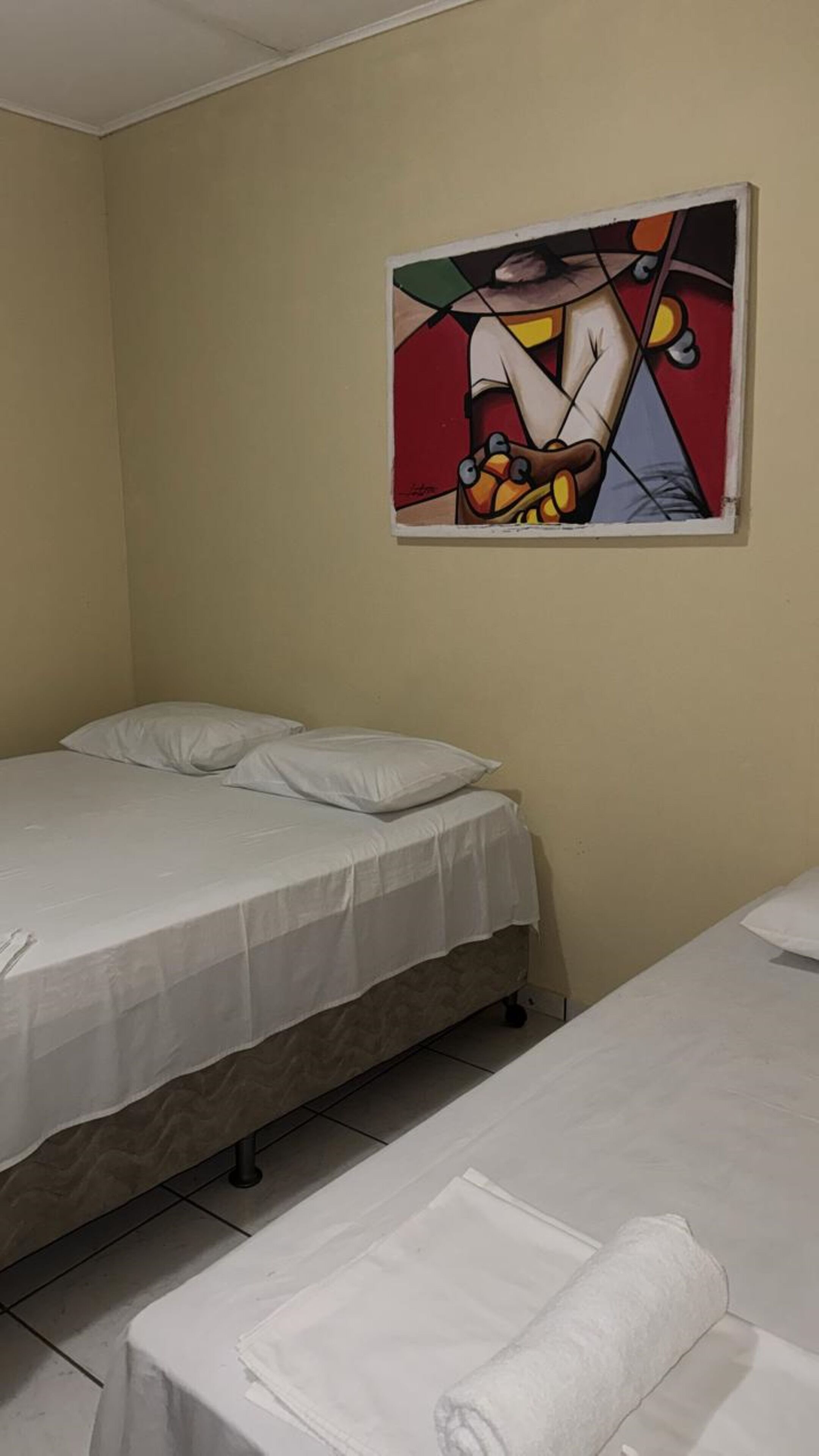 A hotel room with two single beds, a painting on the wall, and a neatly made bed with a rolled towel.