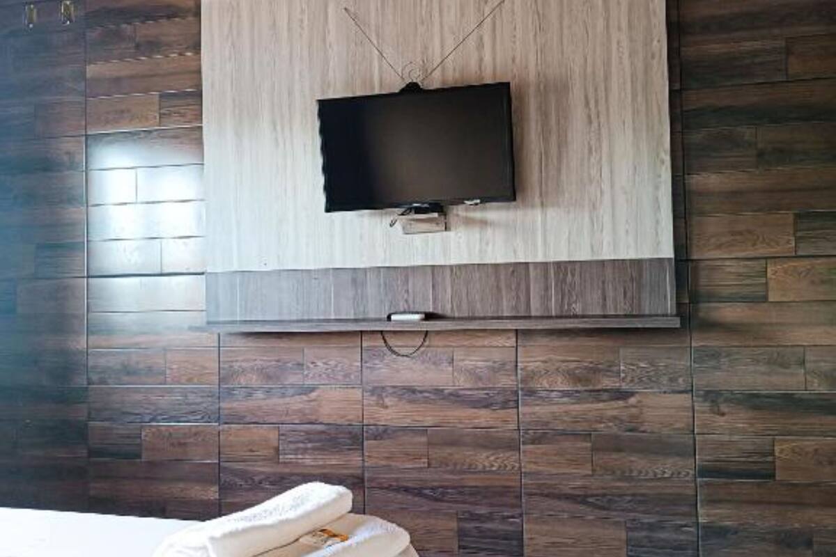 Une chambre d’hôtel avec un grand lit, un téléviseur à écran plat fixé à un mur en bois et un sol carrelé.