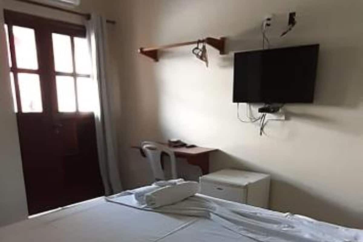 Une chambre d’hôtel avec un lit, un téléviseur fixé au mur et une fenêtre avec des rideaux.