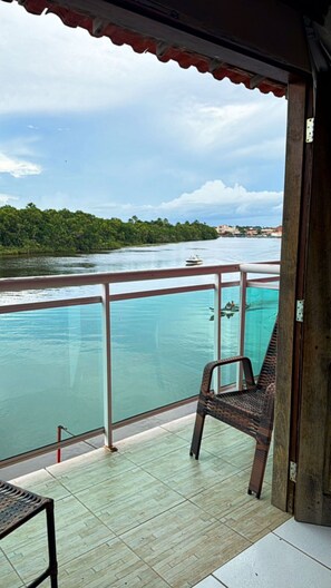 Uma varanda com vista para um corpo de água calma, uma cadeira e uma mesa.