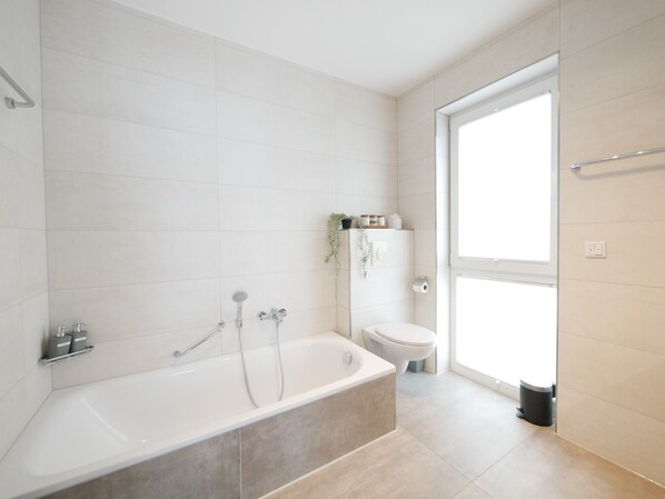 A modern bathroom with a bathtub, toilet, and shower.