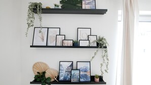 Duas prateleiras pretas fixadas na parede, com obras de arte emolduradas e plantas.