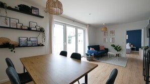 Uma sala de estar moderna com uma mesa de jantar de madeira, cadeiras pretas, um sofá azul e uma grande janela.