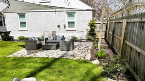 A backyard with a stone patio, outdoor furniture, and a wooden fence.