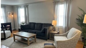 A living room with a dark sofa, a patterned armchair, a wooden coffee table, and a small side table with a lamp.