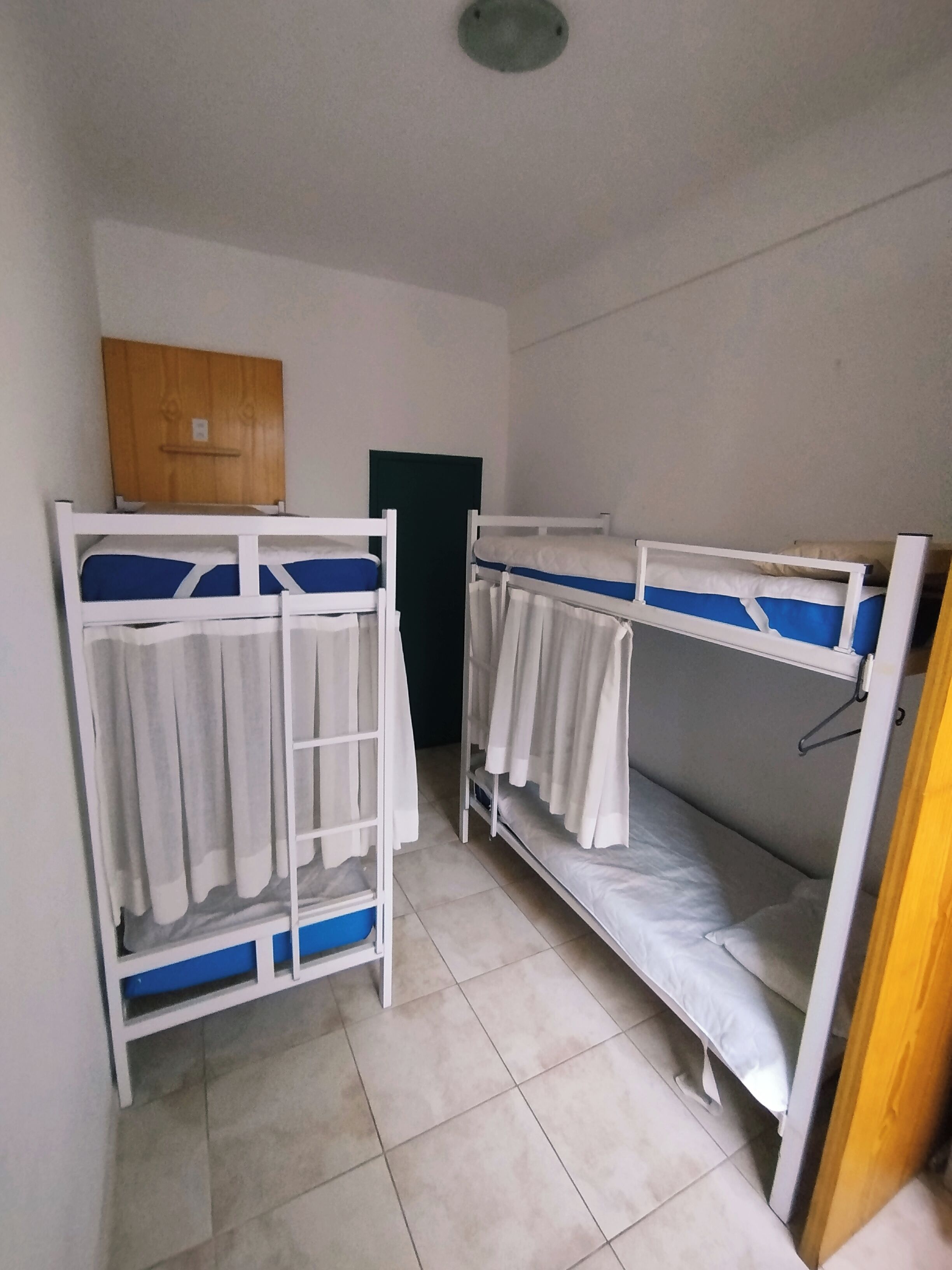 A dormitory room with bunk beds, a wooden cabinet, and a door.