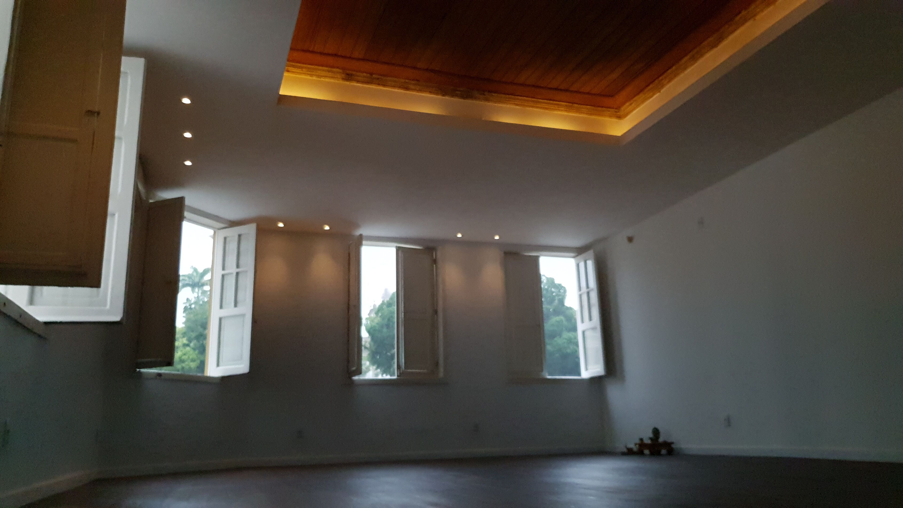 A spacious room with high ceilings, large windows, and a wooden ceiling.