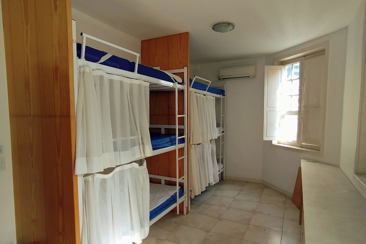 Um quarto com beliches, janela e luminária no teto.