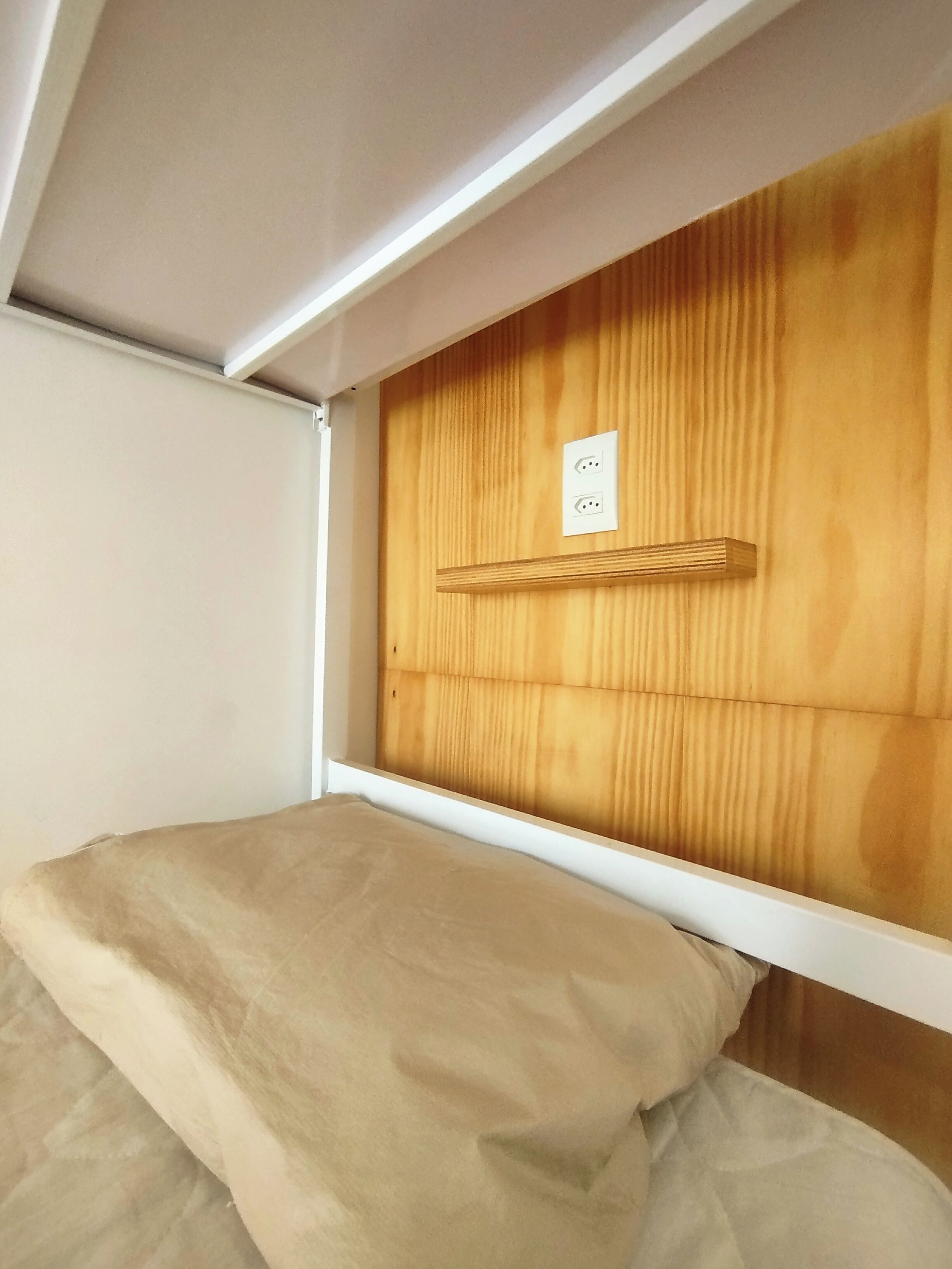 Una cama litera con cabecera de madera y una pared blanca a un lado.