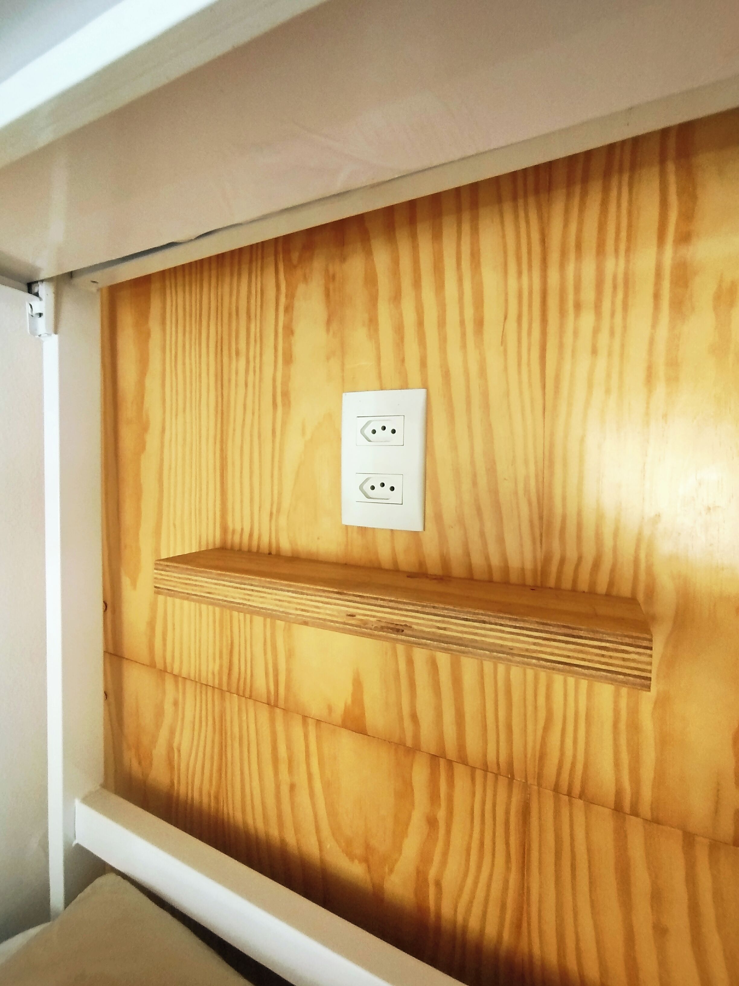 A wooden panel wall with a white shelf and a power outlet.